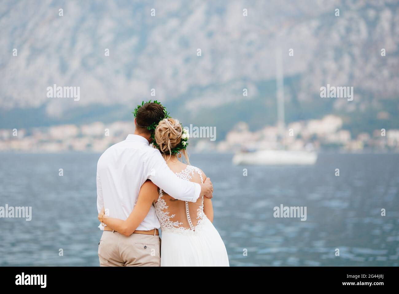 Die Braut und der Bräutigam stehen umarmt auf dem Pier in Die Bucht von Kotor und schauen Sie sich die weiße Yacht an Stockfoto