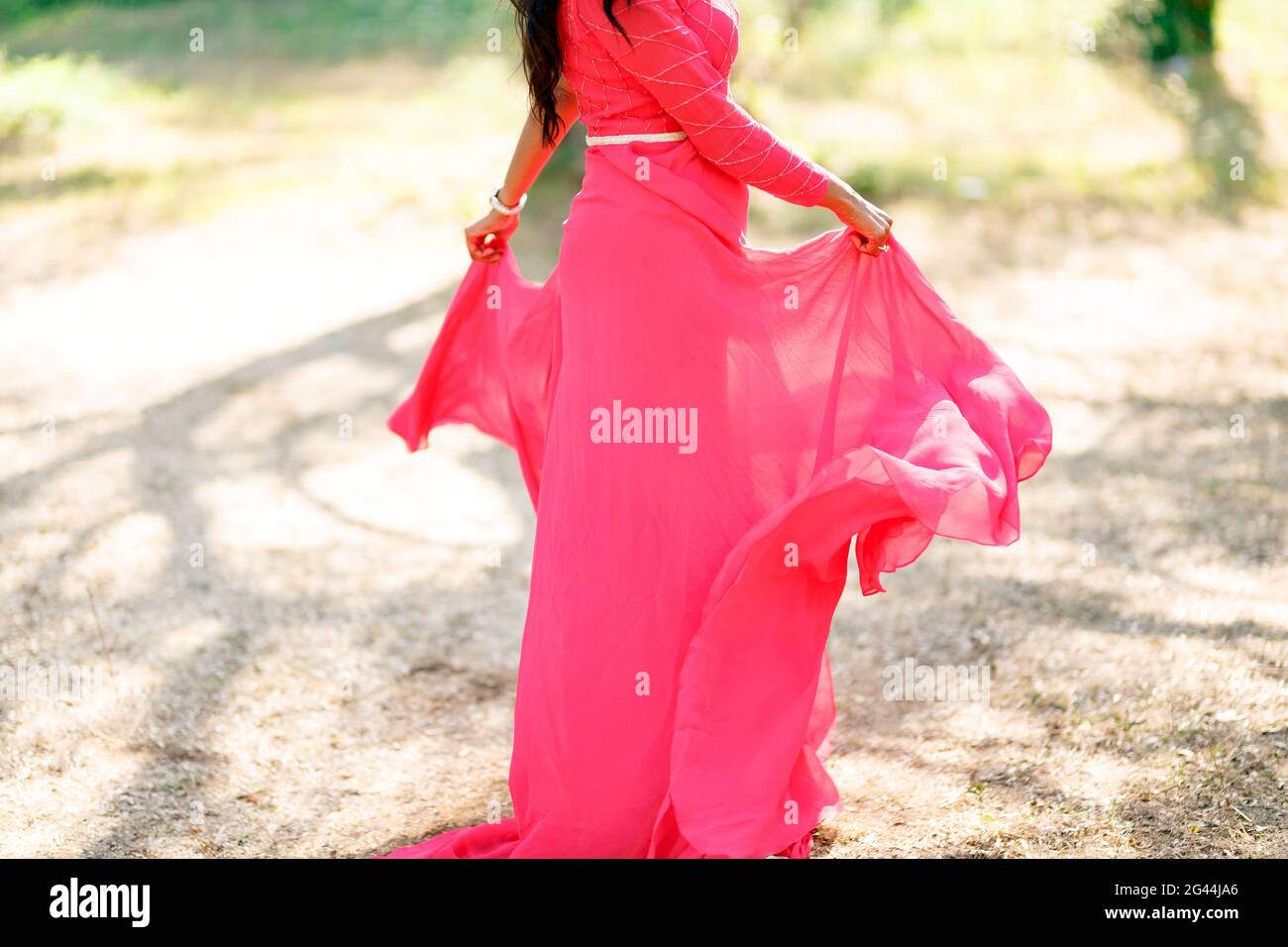 Eine Frau in einem stilvollen hot pink Kleid mit einem Langer Rock dreht sich auf einem trockenen Gras und hält Die Kanten des Rockes mit ihren Händen Stockfoto