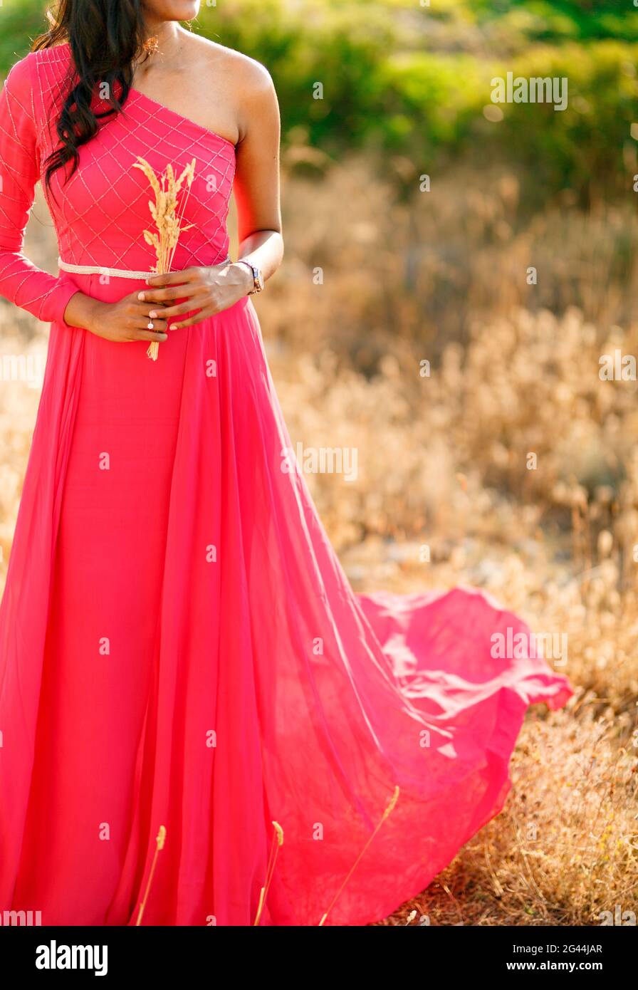 Eine Frau in einem stilvollen hot pink Kleid mit einem Langer Rock steht zwischen den Spikelets und hält Spikelets in Ihre Hände Stockfoto
