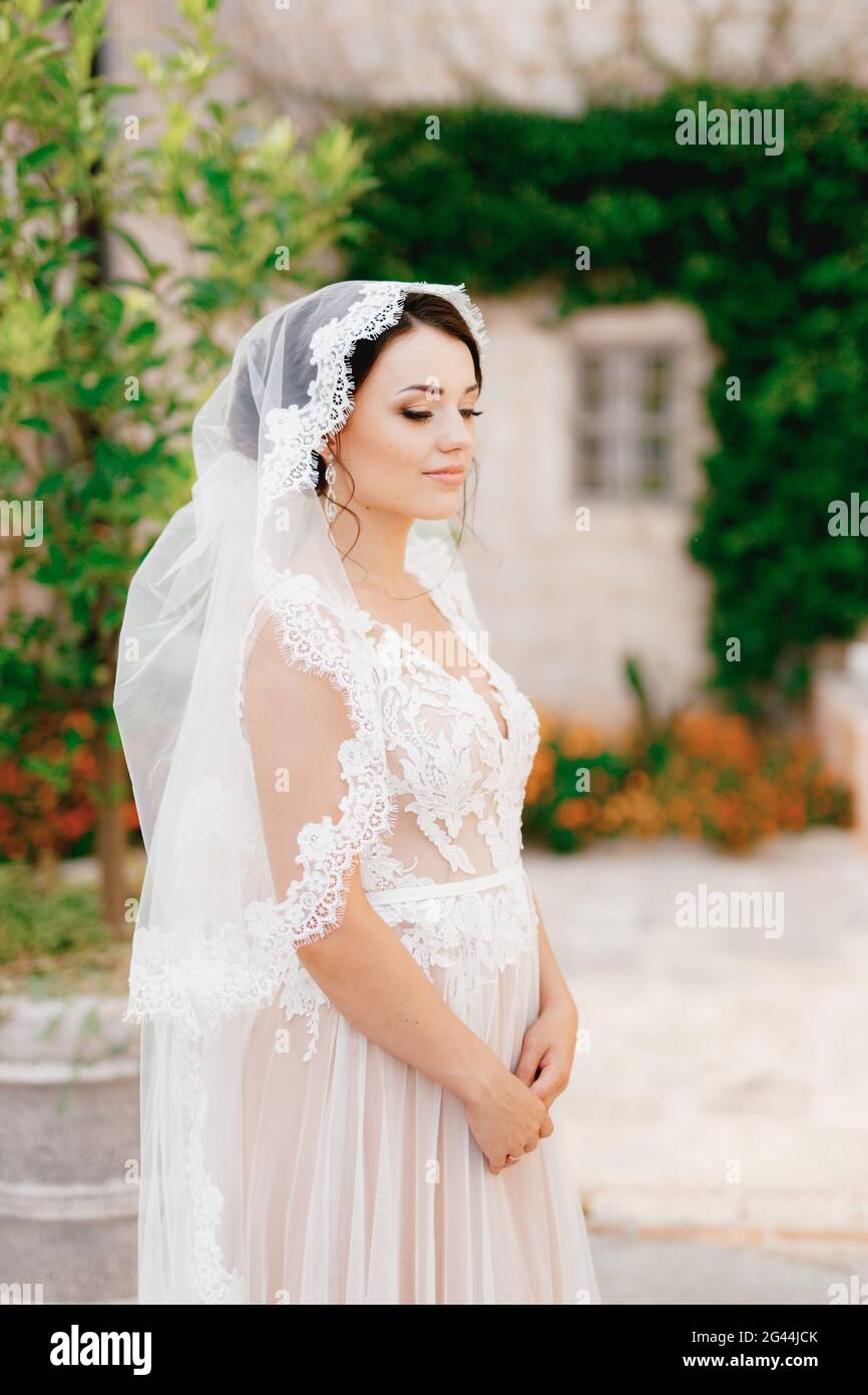 Eine sanfte Braut in einem Schleier aus Spitze steht in der Nähe eines  Weißes Haus, das in der Altstadt mit einer Weinrebe umschlungt ist Der  Perast Stockfotografie - Alamy