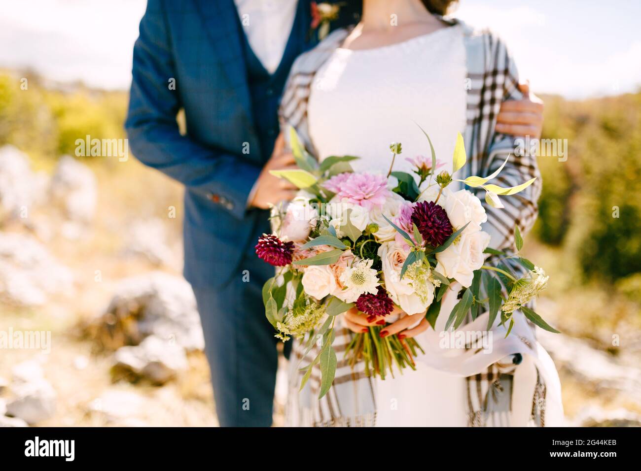 Der Bräutigam umarmt die Schultern der Braut in einem karierten Schal Mit einem schönen Blumenstrauß in ihren Händen Stockfoto