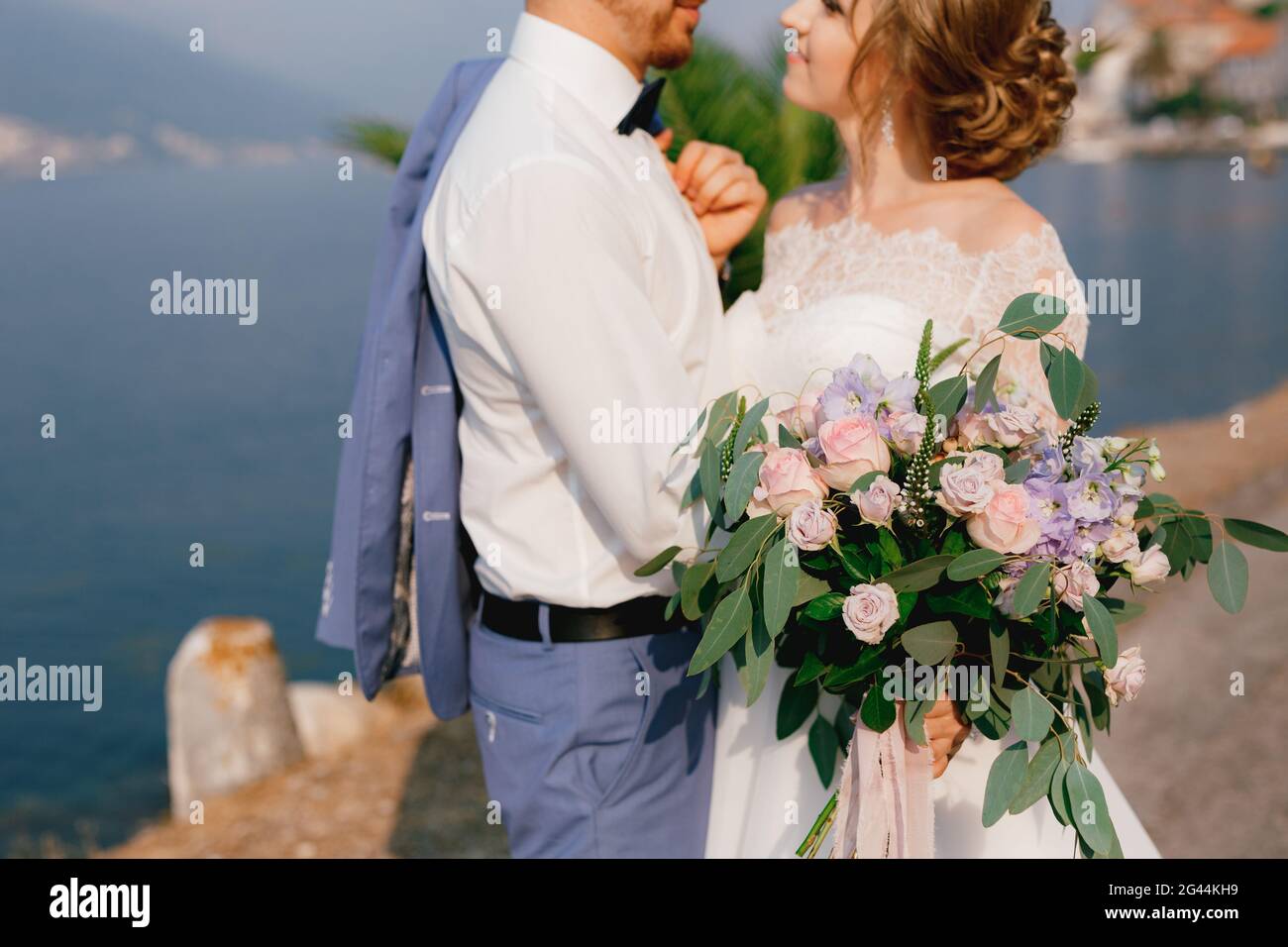 Braut und Bräutigam stehen umarmt am Pier, die Braut hält einen Blumenstrauß in der Hand, aus nächster Nähe Stockfoto