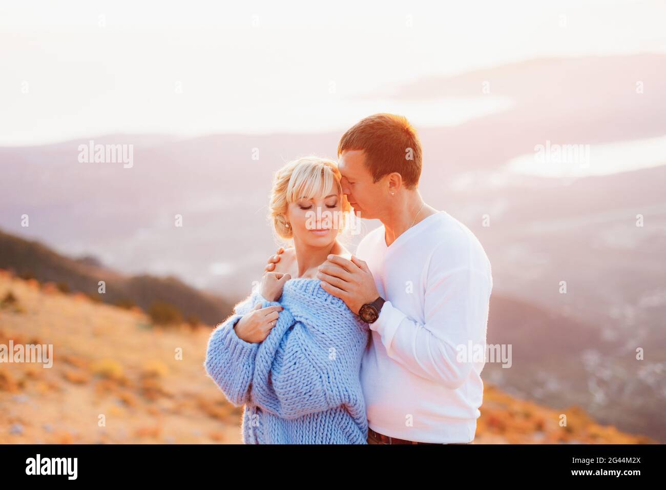 Der Mann umarmt die Frau in einem blauen Pullover an den Schultern Vor dem Hintergrund des Mount Lovcen Stockfoto