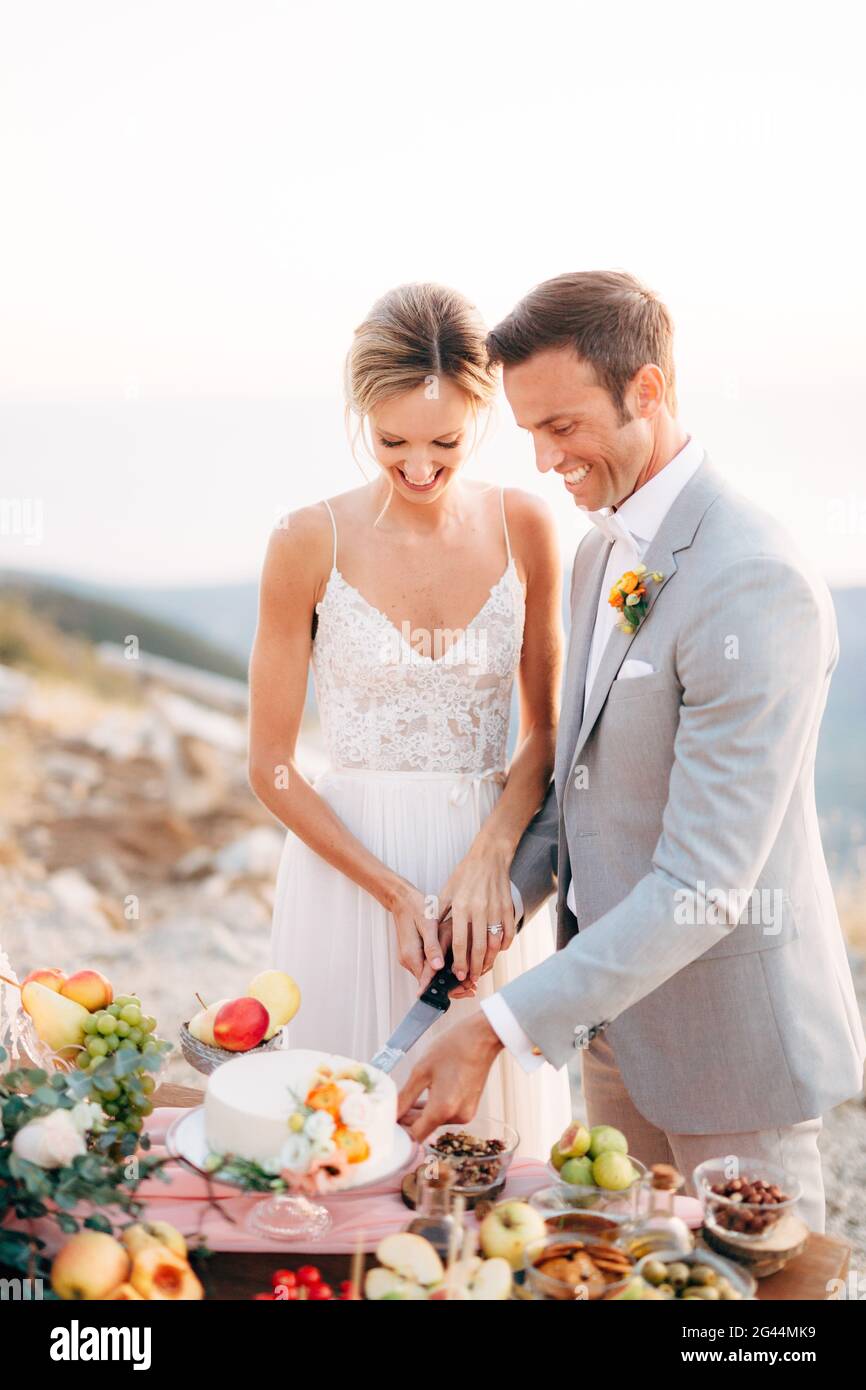 Die Braut und der Bräutigam schneiden einen Kuchen während eines Buffet-Tisch nach der Trauung auf dem Berg Lovcen und Lächelnd Stockfoto