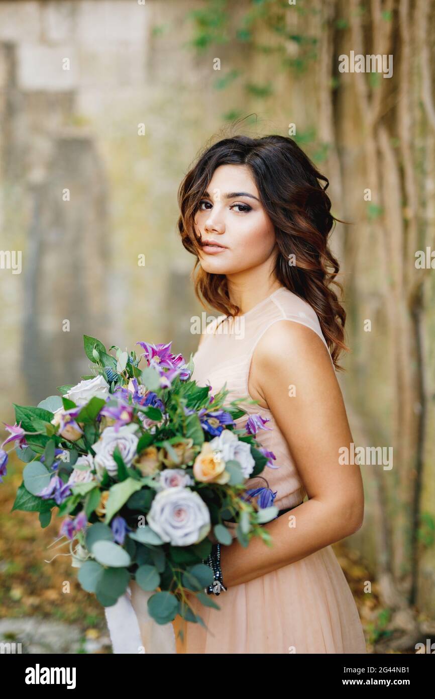 Schöne Braut in einem cremefarbenen Kleid mit einem Bouquet von rosen in ihren Händen Stockfoto