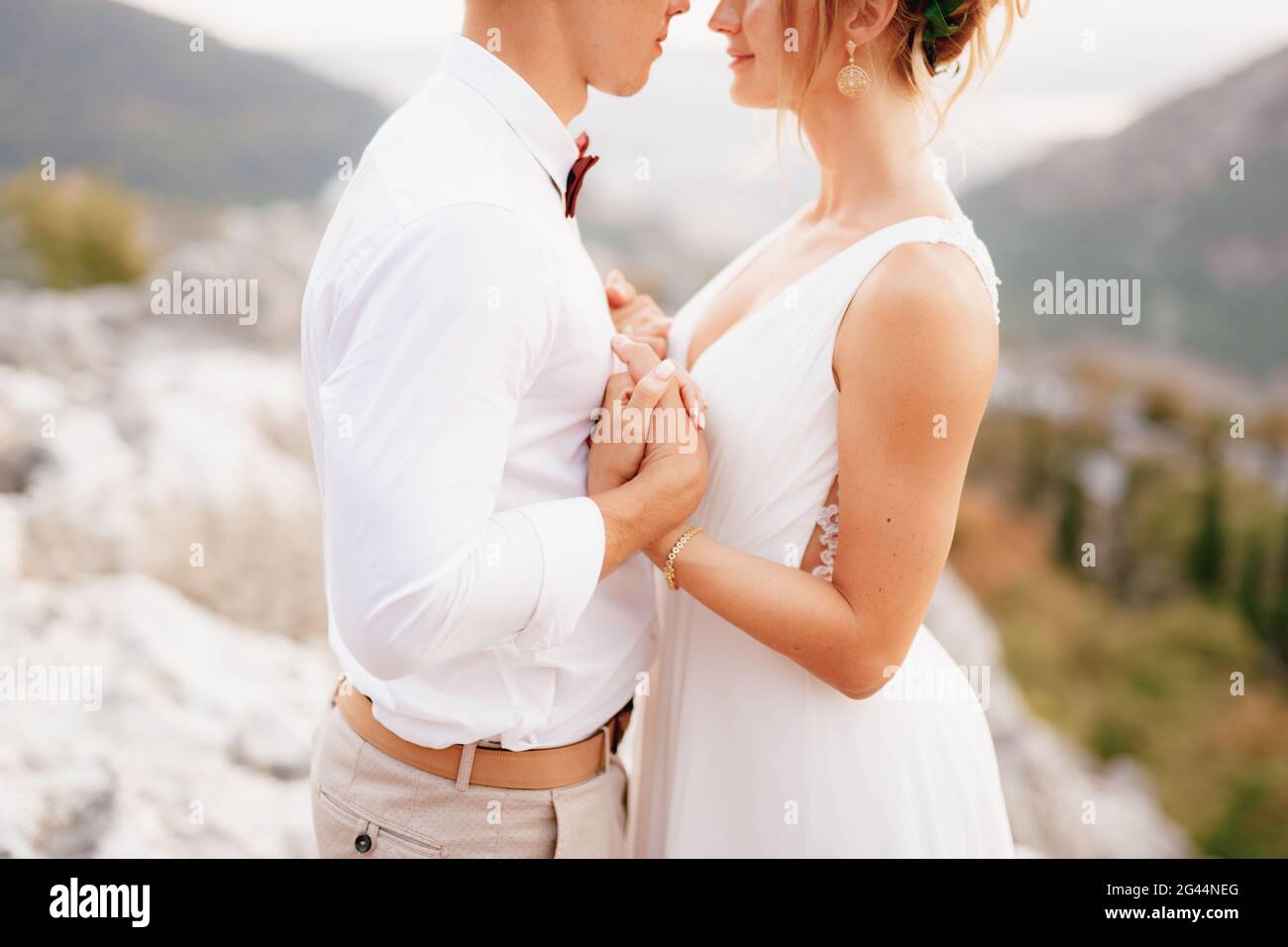 Braut und Bräutigam stehen umarmt zwischen den Bergen und halten sich die Hände fest und schauen einander aus nächster Nähe an Stockfoto
