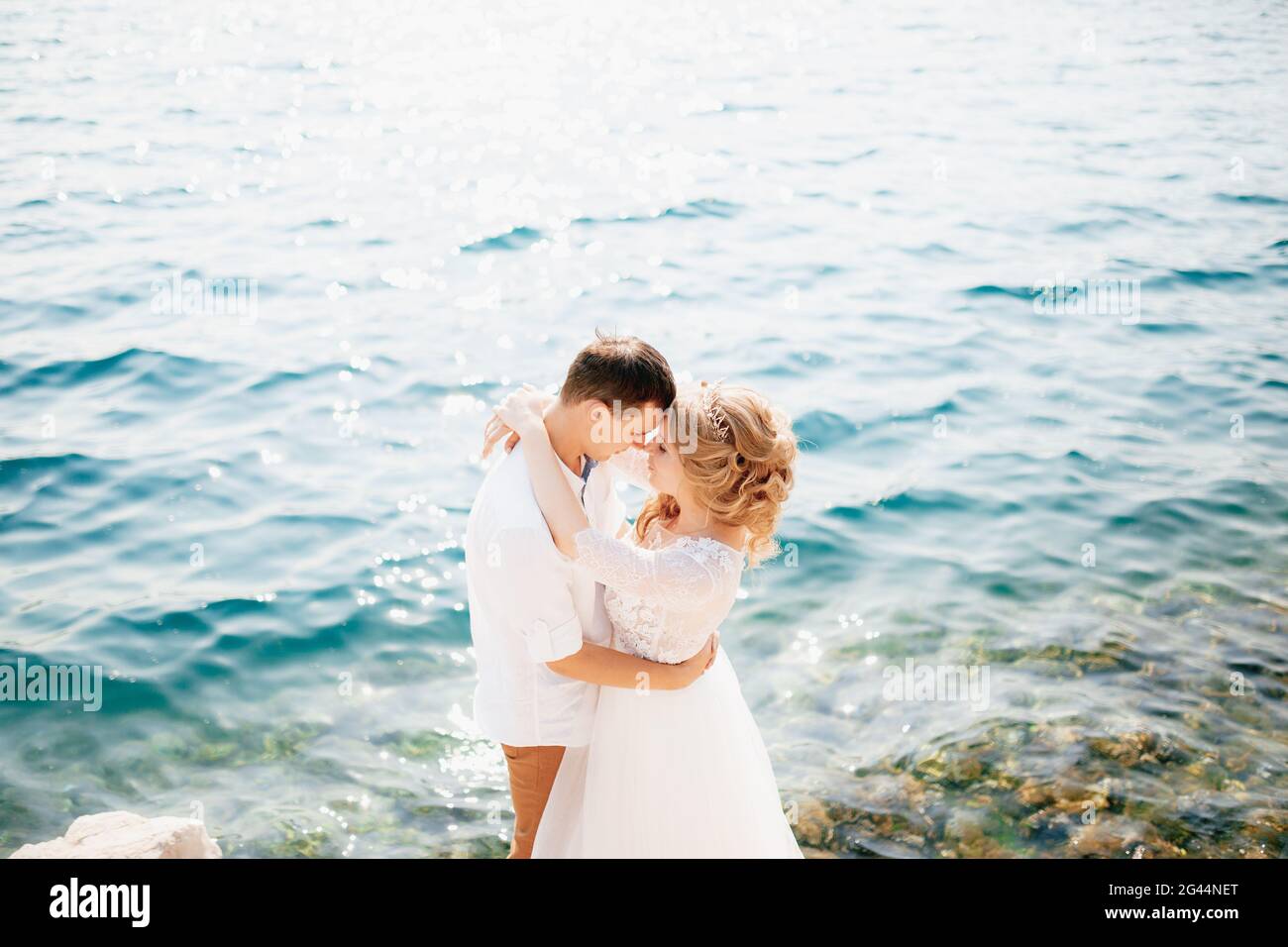 Braut und Bräutigam umarmen sich an der felsigen Küste Und sind dabei, sich zu küssen Stockfoto