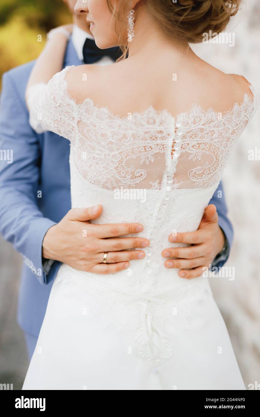 Die Braut und der Bräutigam umarmen sich, die Hände des Bräutigams auf der Taille der Braut in einem Spitzenkleid, Nahaufnahme Stockfoto