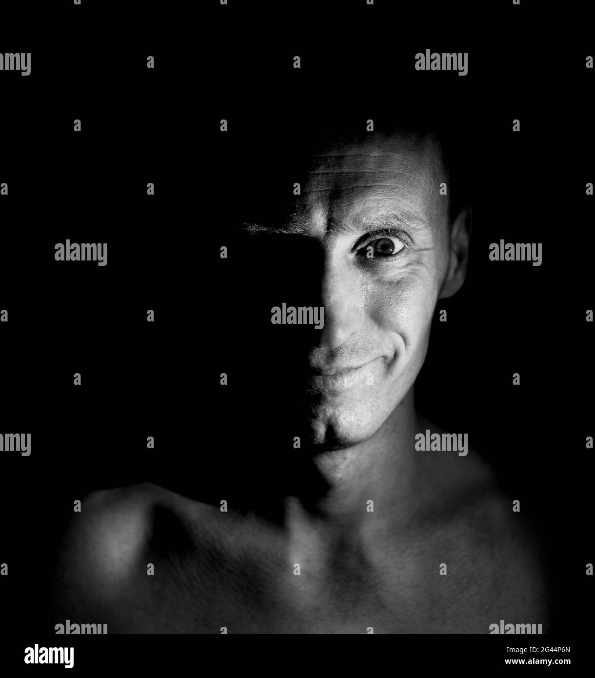 Stilvolle Portrait von Erwachsenen kaukasischen Mann mit freundlichem Lächeln. Das Gesicht des Mannes beleuchtet die Hälfte. Schwarzweiß gedreht, niedrig - Beleuchtung. Stockfoto