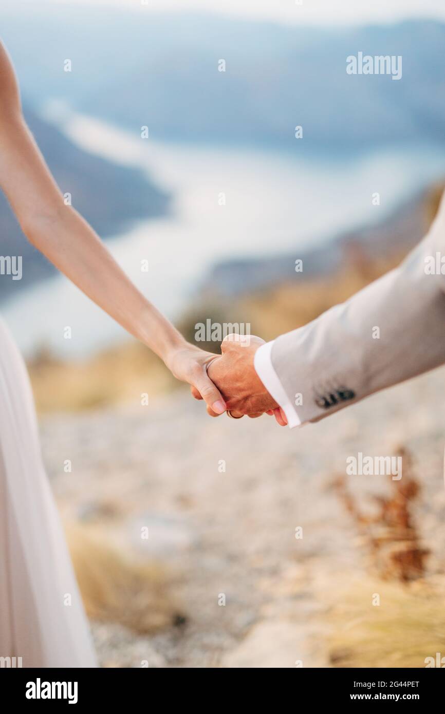 Braut und Bräutigam stehen auf dem Mount Lovcen mit Blick auf die Bucht von Kotor und halten sich gegenseitig die Hände aus nächster Nähe Stockfoto