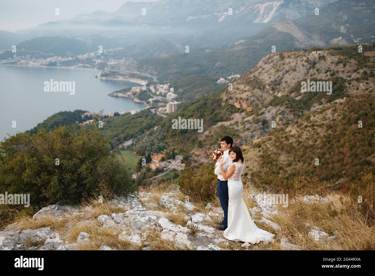 Das Brautpaar umarmt sich vor dem Hintergrund eines Panoramas auf die Stadt Budva, die Berge und das Meer Stockfoto