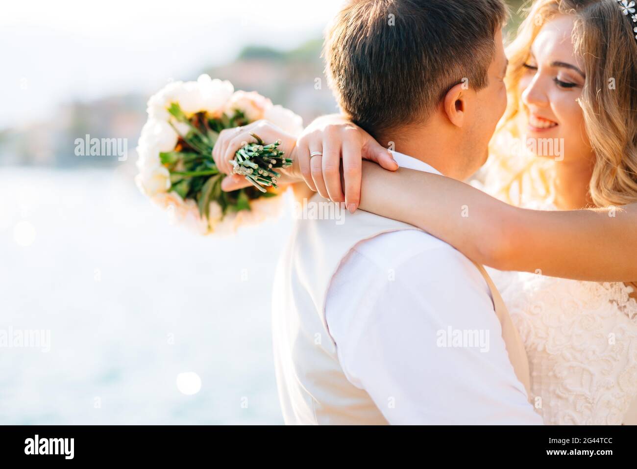 Die Braut umarmt den Bräutigam und hält einen Blumenstrauß in den Händen auf dem Pier in der Bucht von Kotor, Nahaufnahme Stockfoto