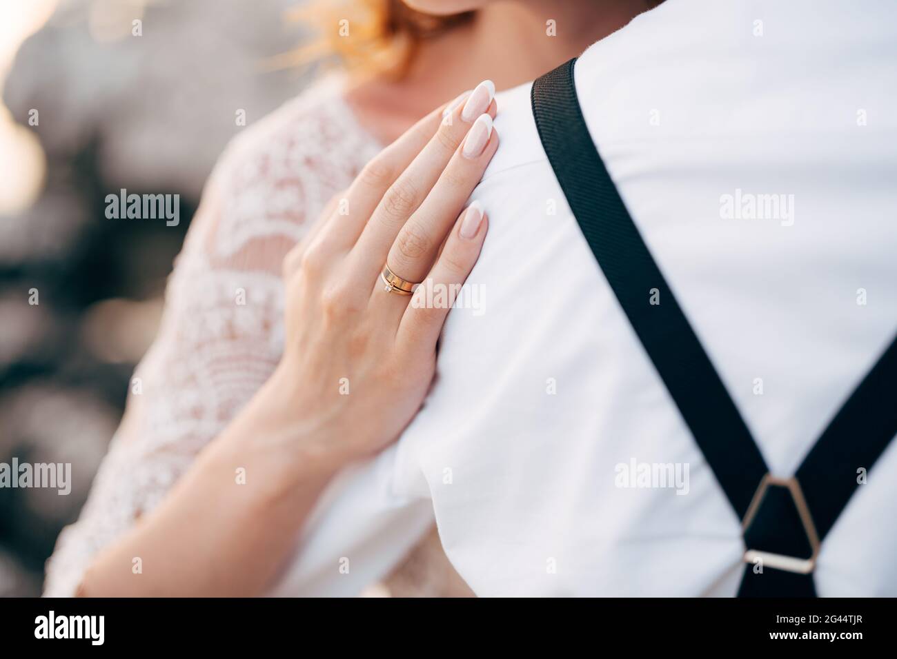 Braut in weißem Spitzenkleid legte ihre Hand auf die Schulter des Bräutigams in weißem Hemd. Nahaufnahme Stockfoto
