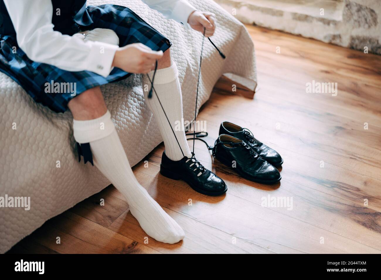 Vorbereitung auf eine schottische Hochzeit. Mann in einem Kilt, Sporran und hohen Socken sitzt auf dem Bett und binden lange Schnürsenkel an seine Schuhe Stockfoto