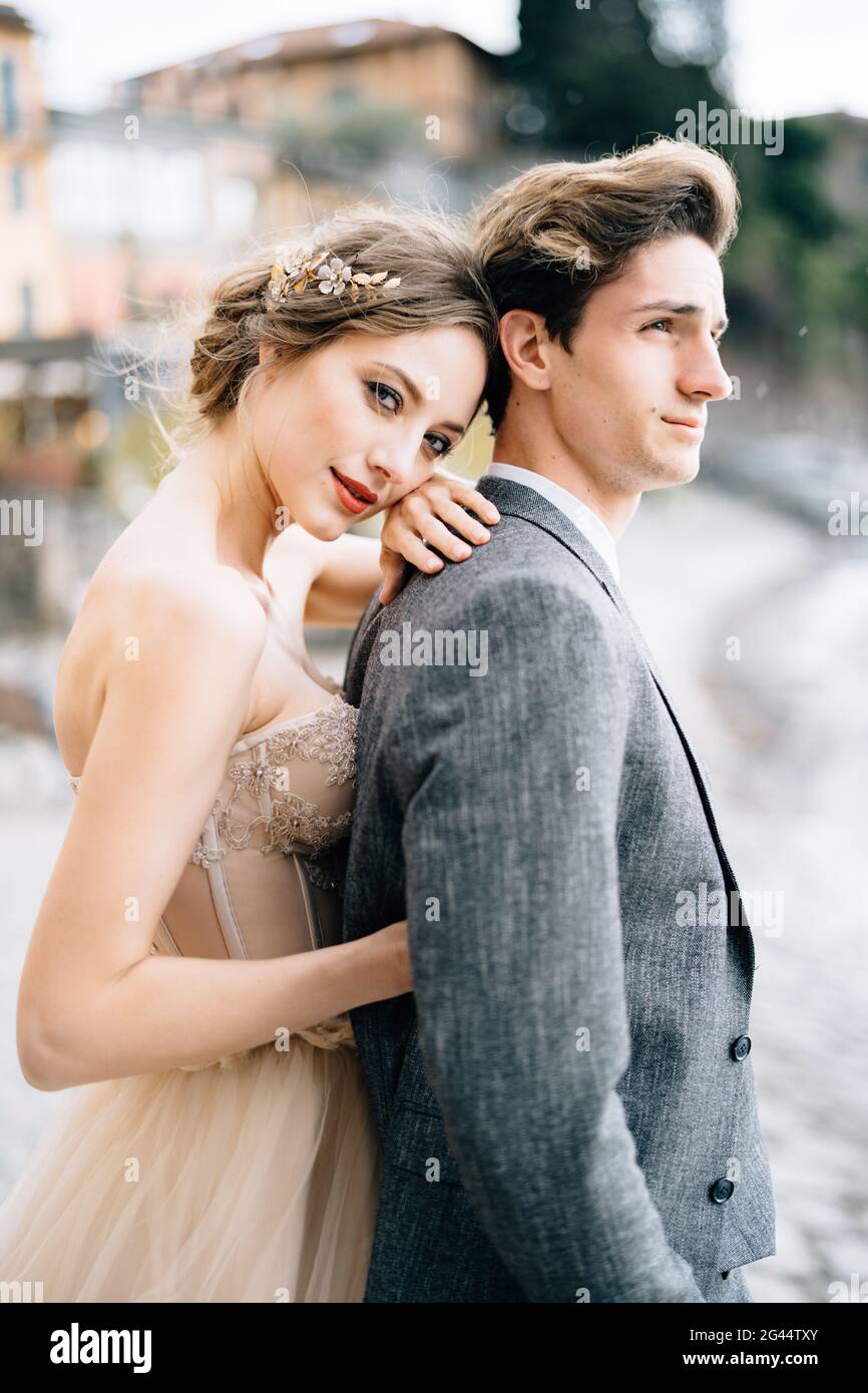 Nachdenkliche Braut umarmt Bräutigam von hinten, während sie auf dem steht Promenade des Comer Sees Stockfoto