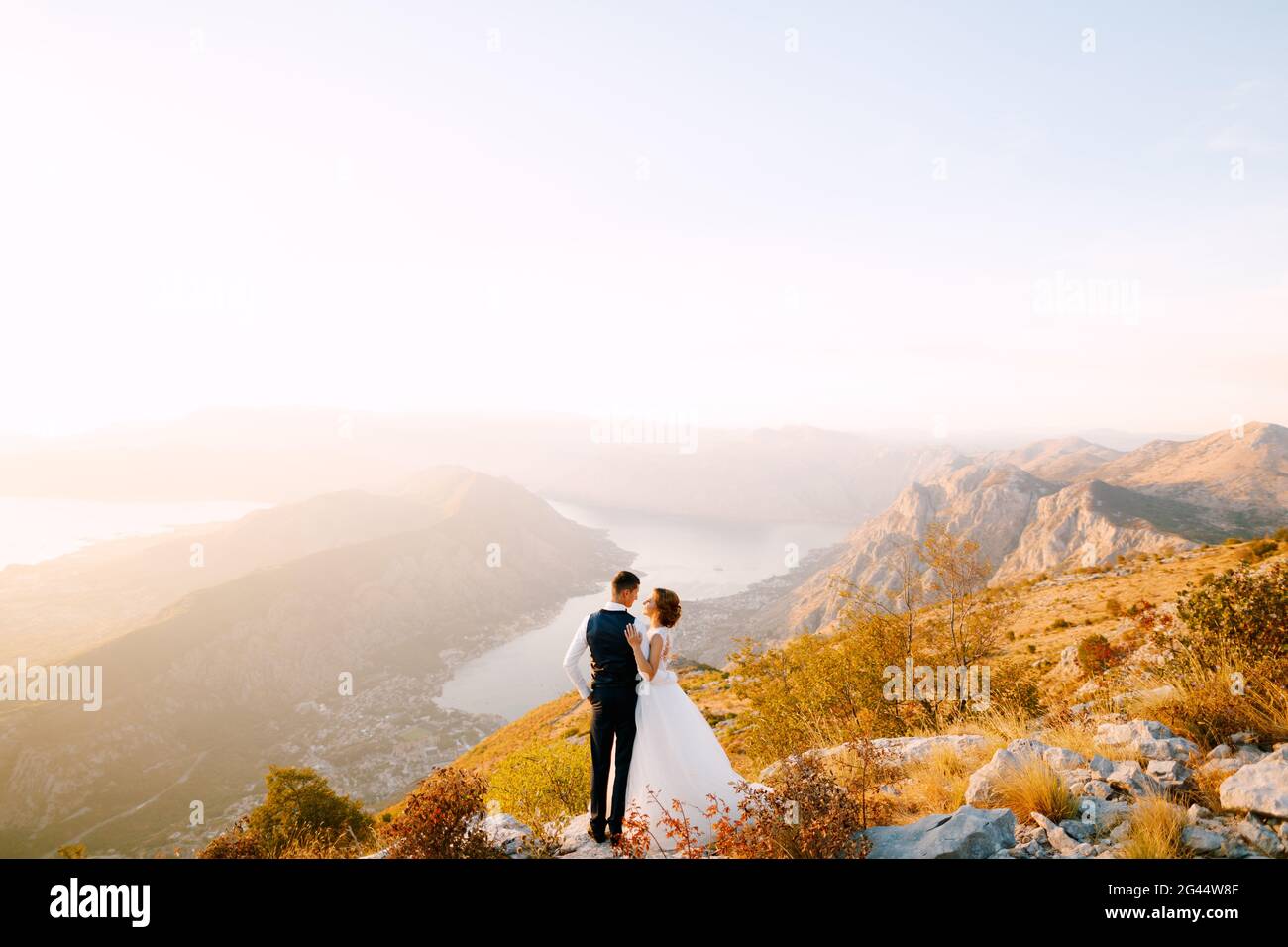 Die Braut und der Bräutigam stehen auf dem Gipfel des Mount Lovcen mit Blick auf die Bucht von Kotor, lächeln und umarmen sie zärtlich Stockfoto