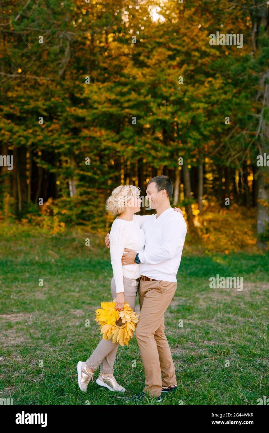 Mann in hellen Kleidern lächelt umarmt Frau mit einem Blumenstrauß Von gelben Blättern im Herbstwald Stockfoto