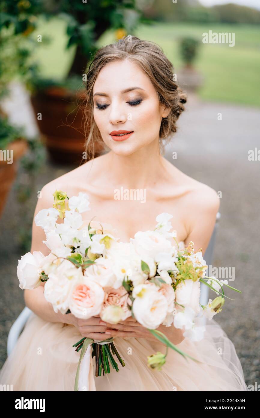 Die Braut schloss ihre Augen in einem schönen Kleid mit einem Blumenstrauß vor dem Hintergrund eines grünen Baumes in einer Wanne. Comer See Stockfoto