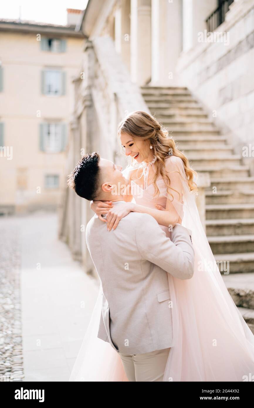 Bräutigam hält die Braut in den Armen nahe der Treppe eines alten Gebäudes in Bergamo, Italien. Nahaufnahme Stockfoto