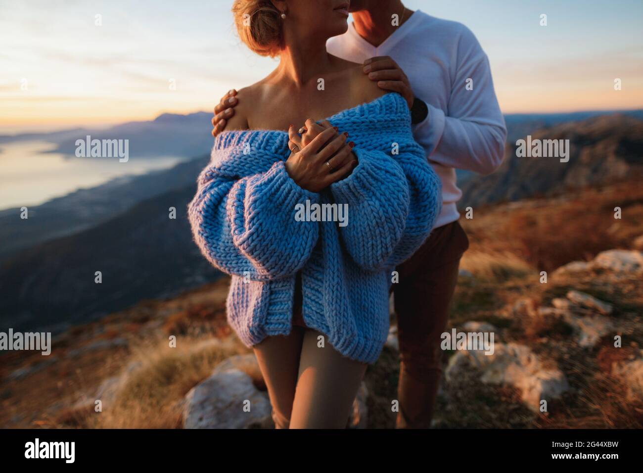Der Mann umarmt eine Frau in einem blauen Pullover an den Schultern auf dem Hintergrund der Berge. Nahaufnahme Stockfoto