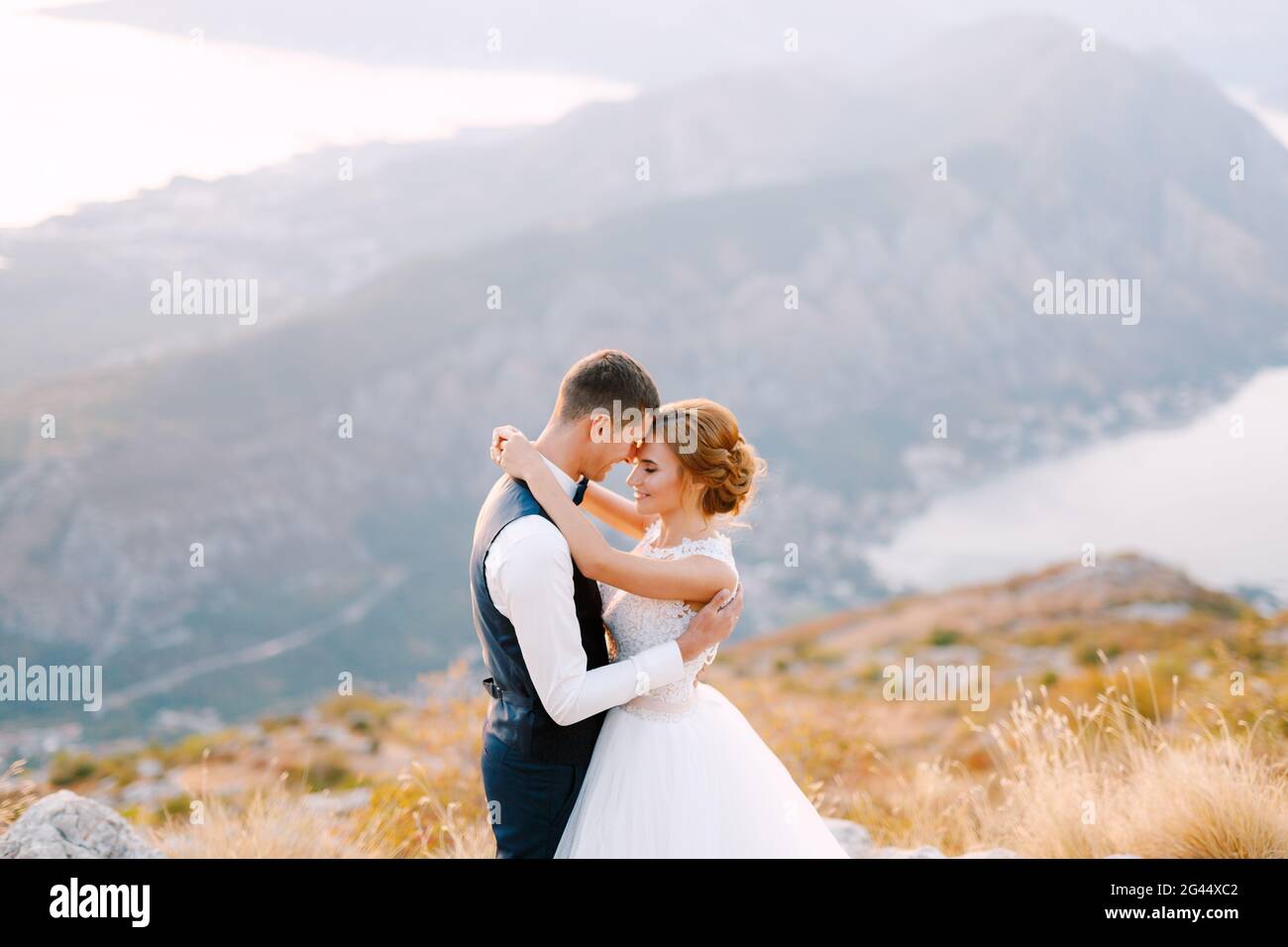 Die Braut und der Bräutigam stehen auf dem Gipfel des Mount Lovcen mit Blick auf die Bucht von Kotor und umarmen sich liebevoll aus nächster Nähe Stockfoto