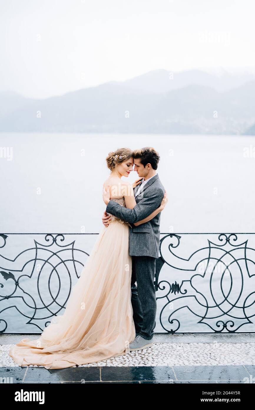 Das Brautpaar umarmt sich in der Nähe eines schmiedeeisernen Zauns vor dem Hintergrund von Comer See Stockfoto