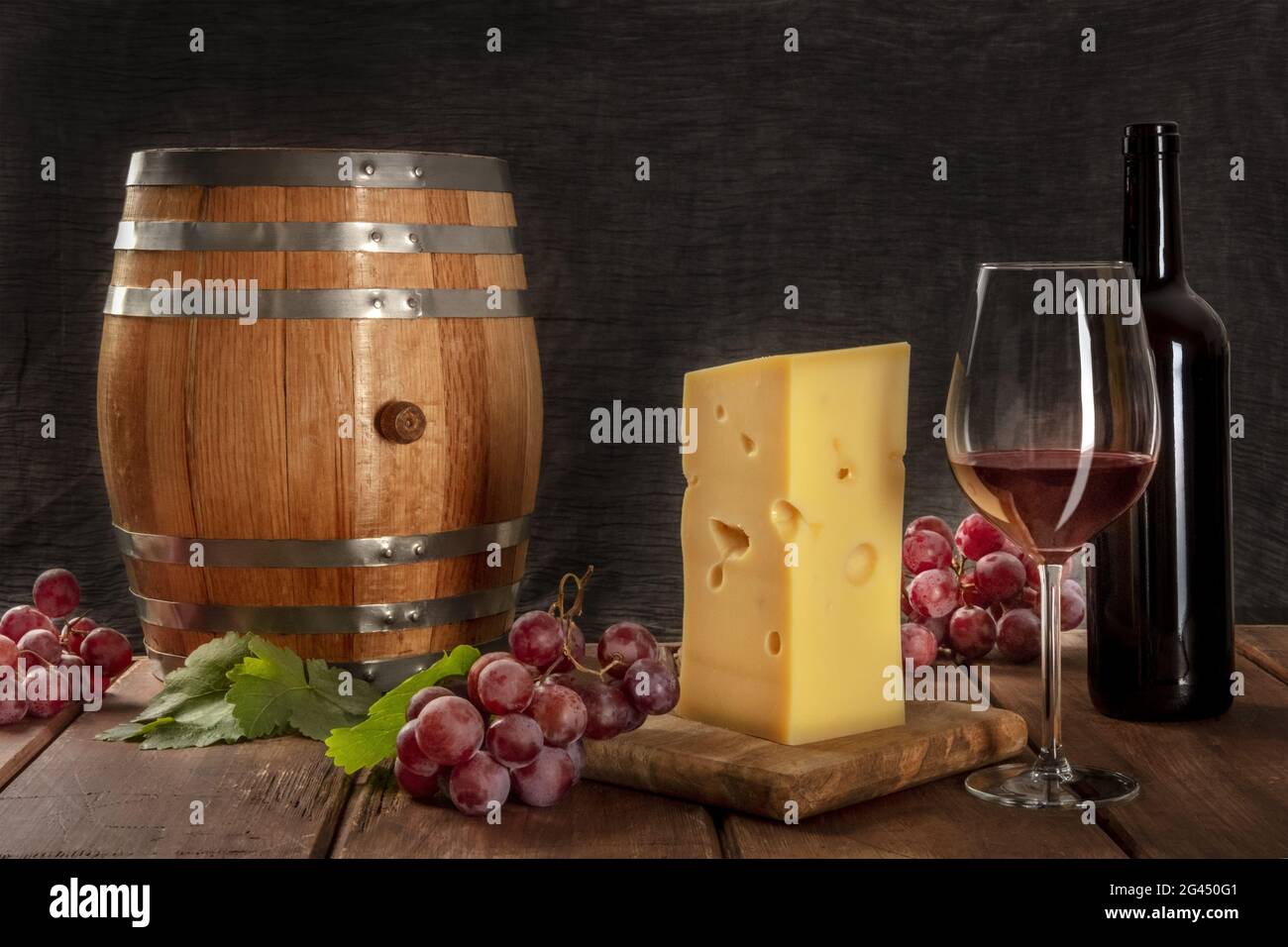 Ein Glas Rotwein mit einer Flasche, ein Weinfass, ein großes Stück Cheesse,  Trauben und Weinblätter Stockfotografie - Alamy