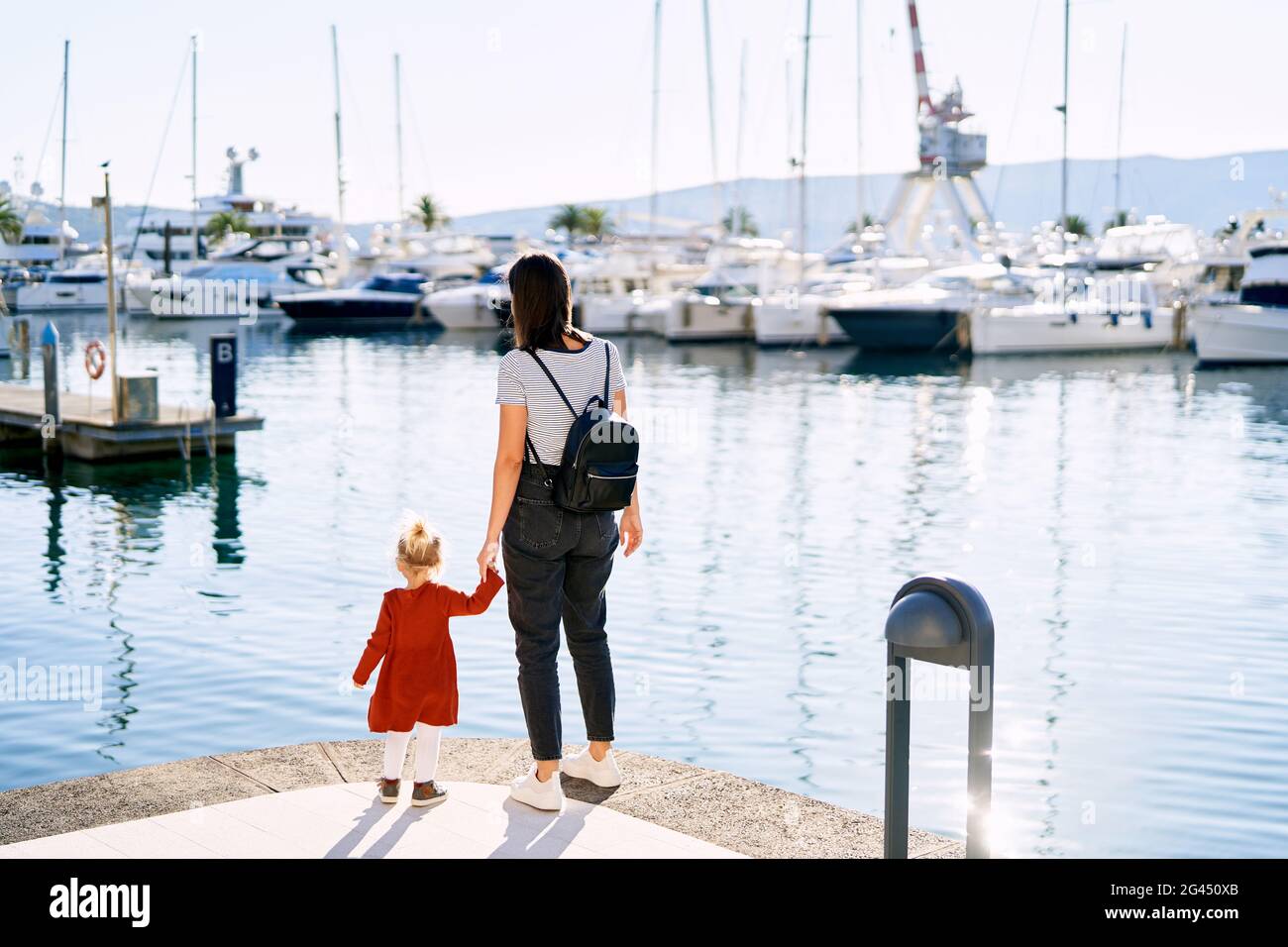 Mutter hält die Hand ihrer Tochter und schaut auf Boote In Porto Montenegro Stockfoto