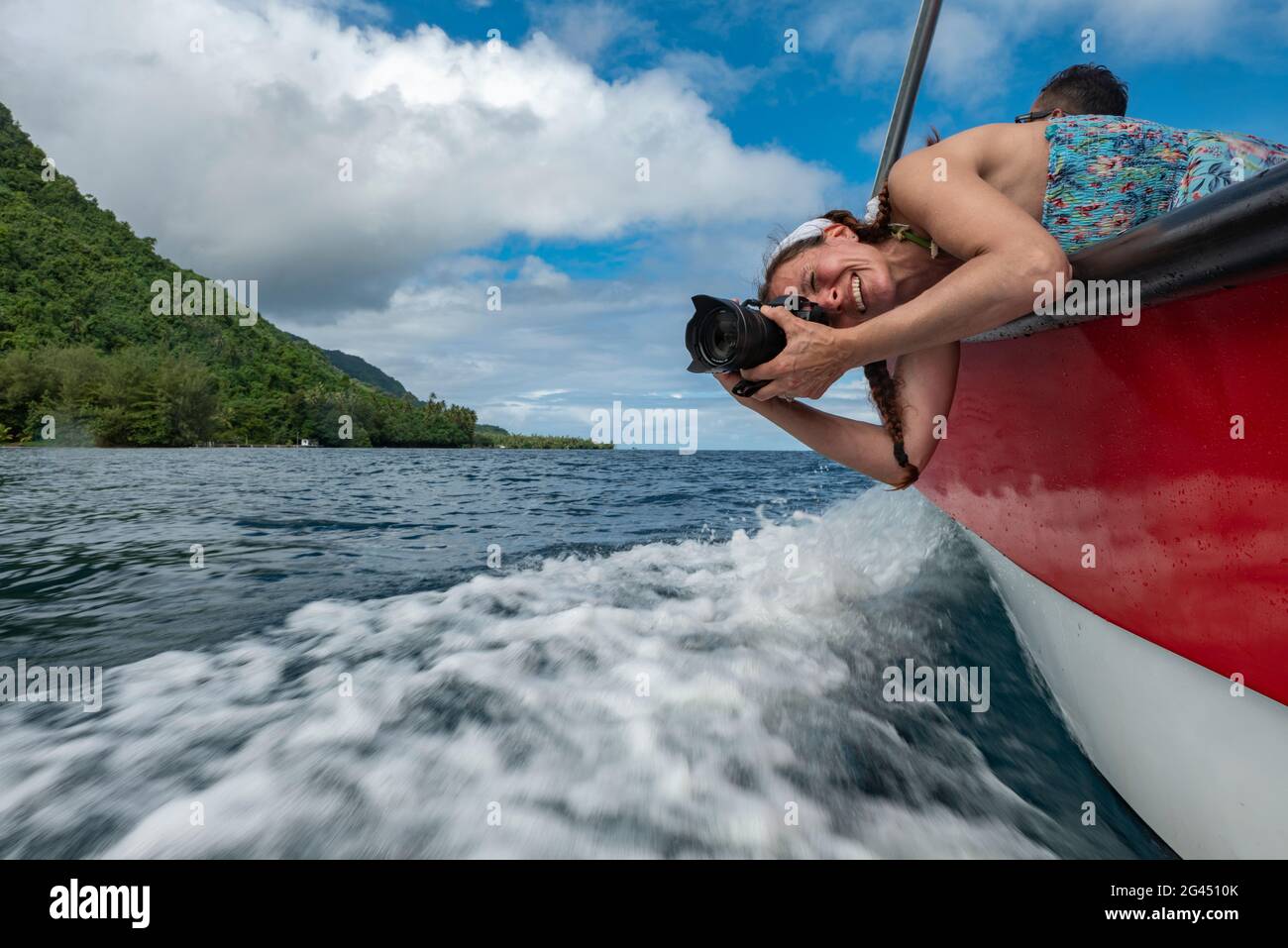 Lächelnde Frau mit Kamera lehnt sich über das Ausflugsboot, um Wellen zu fotografieren, Tahiti Iti, Tahiti, Windward Islands, Französisch-Polynesien, Südpazifik Stockfoto