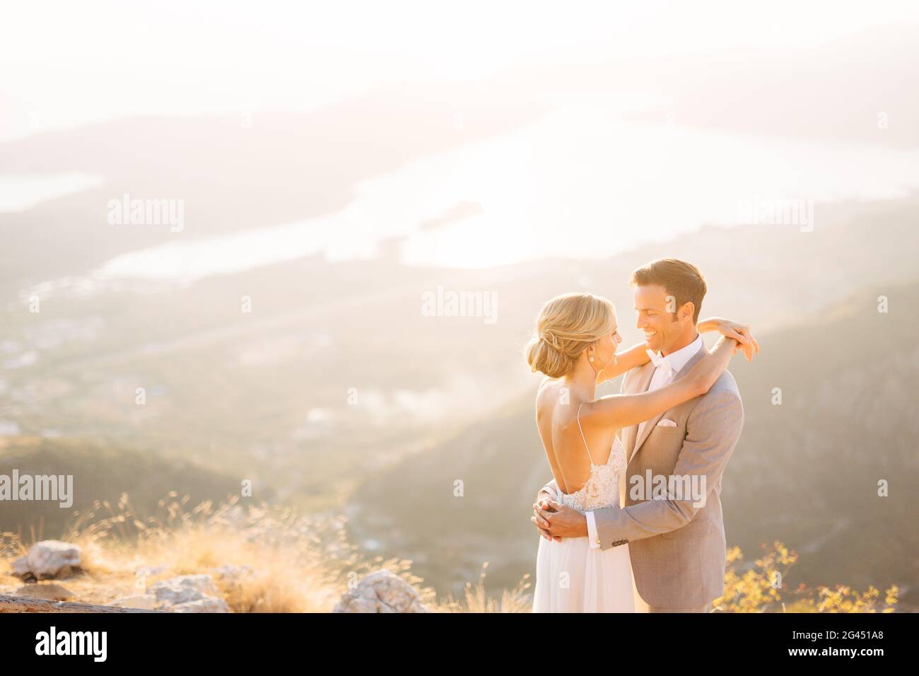Die Braut und der Bräutigam stehen auf dem Gipfel des Mount Lovcen mit Blick auf die Bucht von Kotor, lächeln und umarmen sie zärtlich Stockfoto