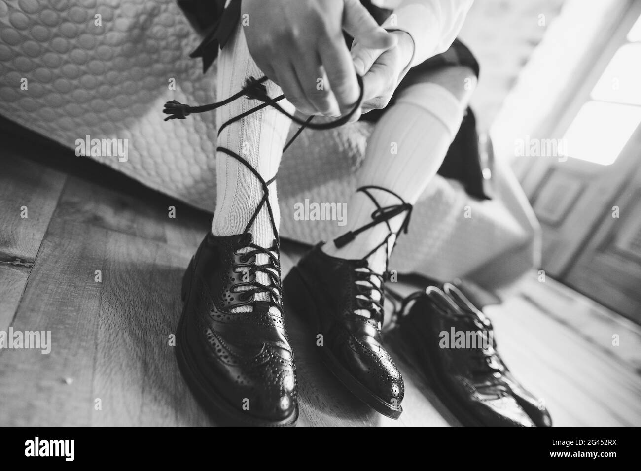 Vorbereitung auf eine schottische Hochzeit. Mann in einem Kilt und hohen  Socken sitzt auf dem Bett und binden lange Schnürsenkel an seine Schuhe.  Schwarz und WH Stockfotografie - Alamy