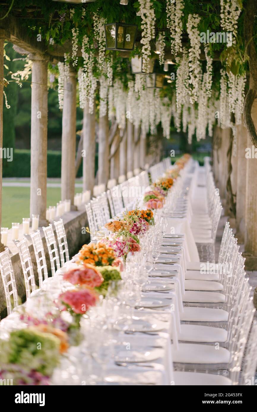 Hochzeitsessen Tischempfang. Ein sehr langer Tisch für Gäste mit weißer Tischdecke, Blumenarrangements, Glas-Kunststoff-Transpa Stockfoto