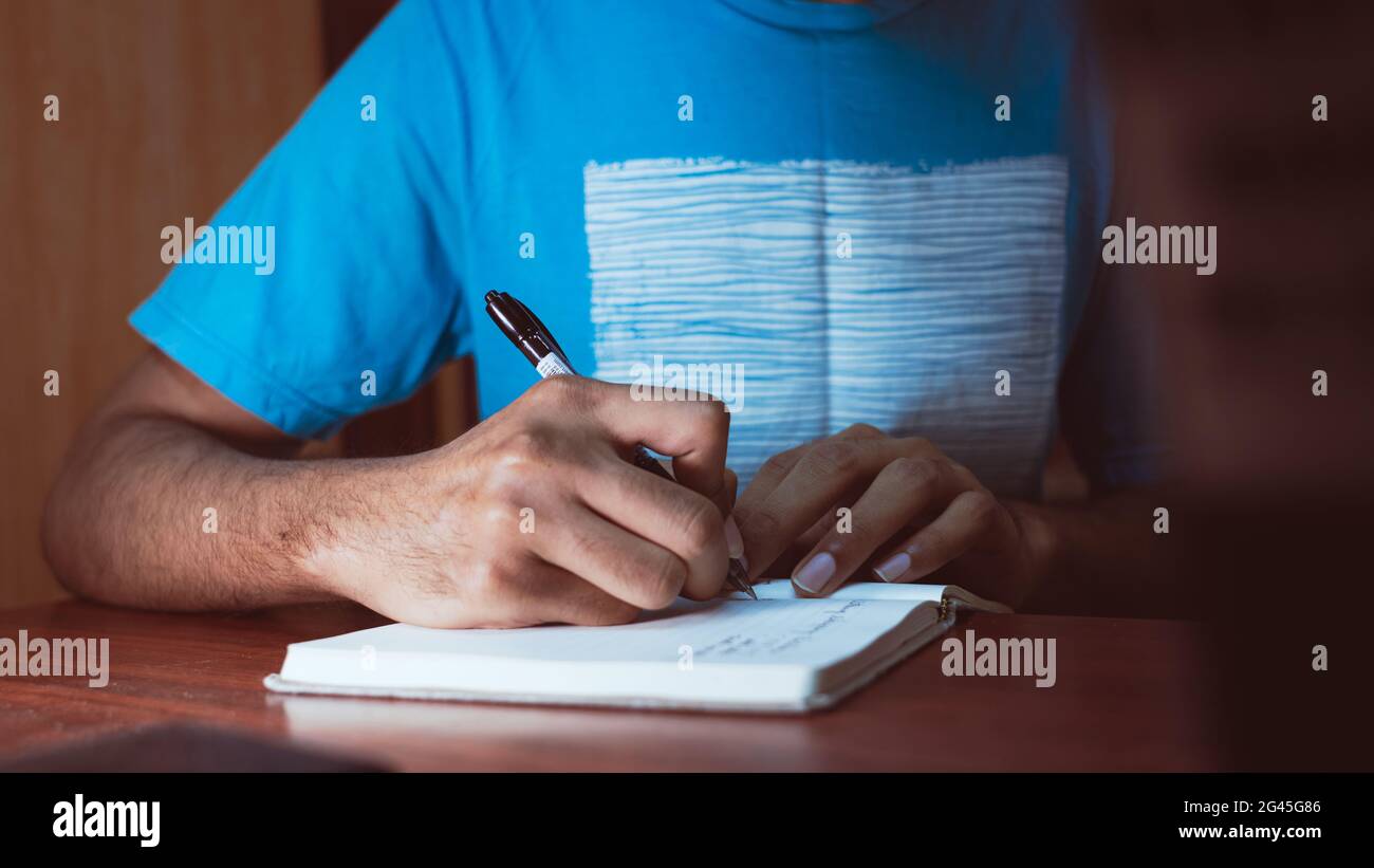 Ein junger erwachsener Mann, der ein Tagebuch auf einem kleinen Notizbuch schreibt. Stockfoto