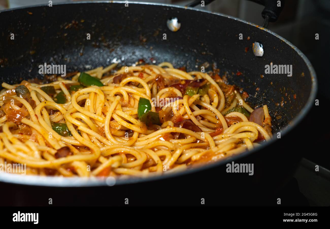 Selektive Konzentration von Spaghetti, die in einer Pfanne mit grünen Paprika, Zwiebeln, roten Chilischoten und jalapeños in Pomodoro-Sauce gekocht werden. Stockfoto