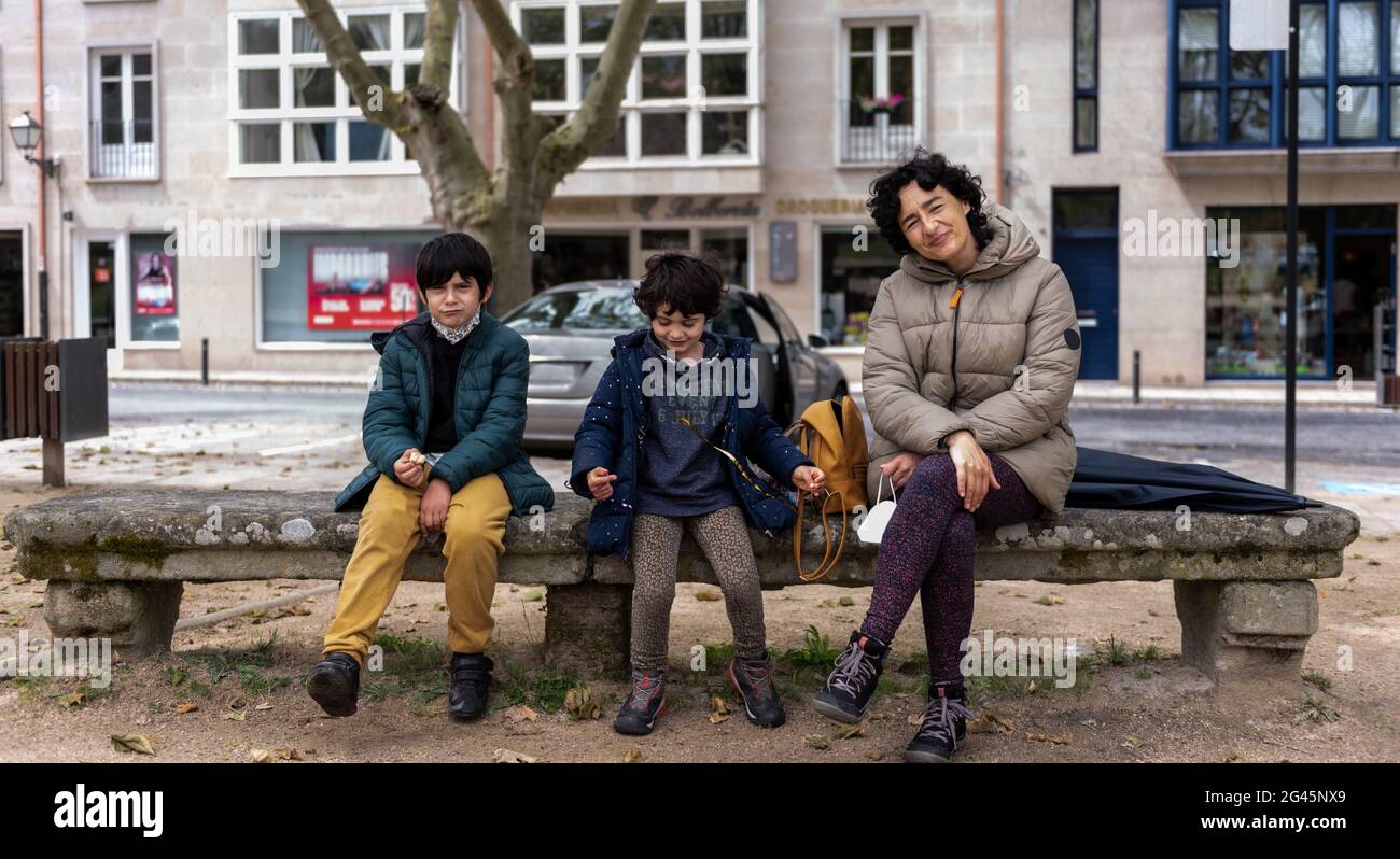 Junge Mutter, die mit ihren zwei Söhnen auf einer Steinbank in einem Stadtpark sitzt Stockfoto