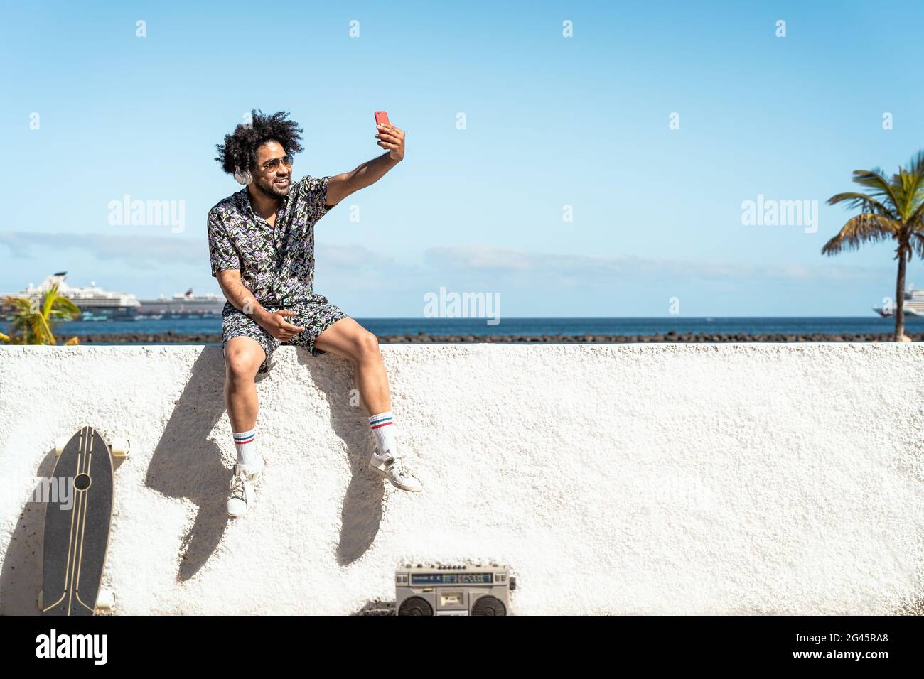 Junger Latein-Mann, der Spaß hat, Selfie mit dem mobilen Smartphone zu machen Während der Sommerferien Musik mit Kopfhörern und Boombox hören Stockfoto Junger Latein-Mann, der Spaß hat, Selfie mit dem mobilen Smartphone zu machen Während der Sommerferien Musik mit Kopfhörern und Boombox hören Stockfoto