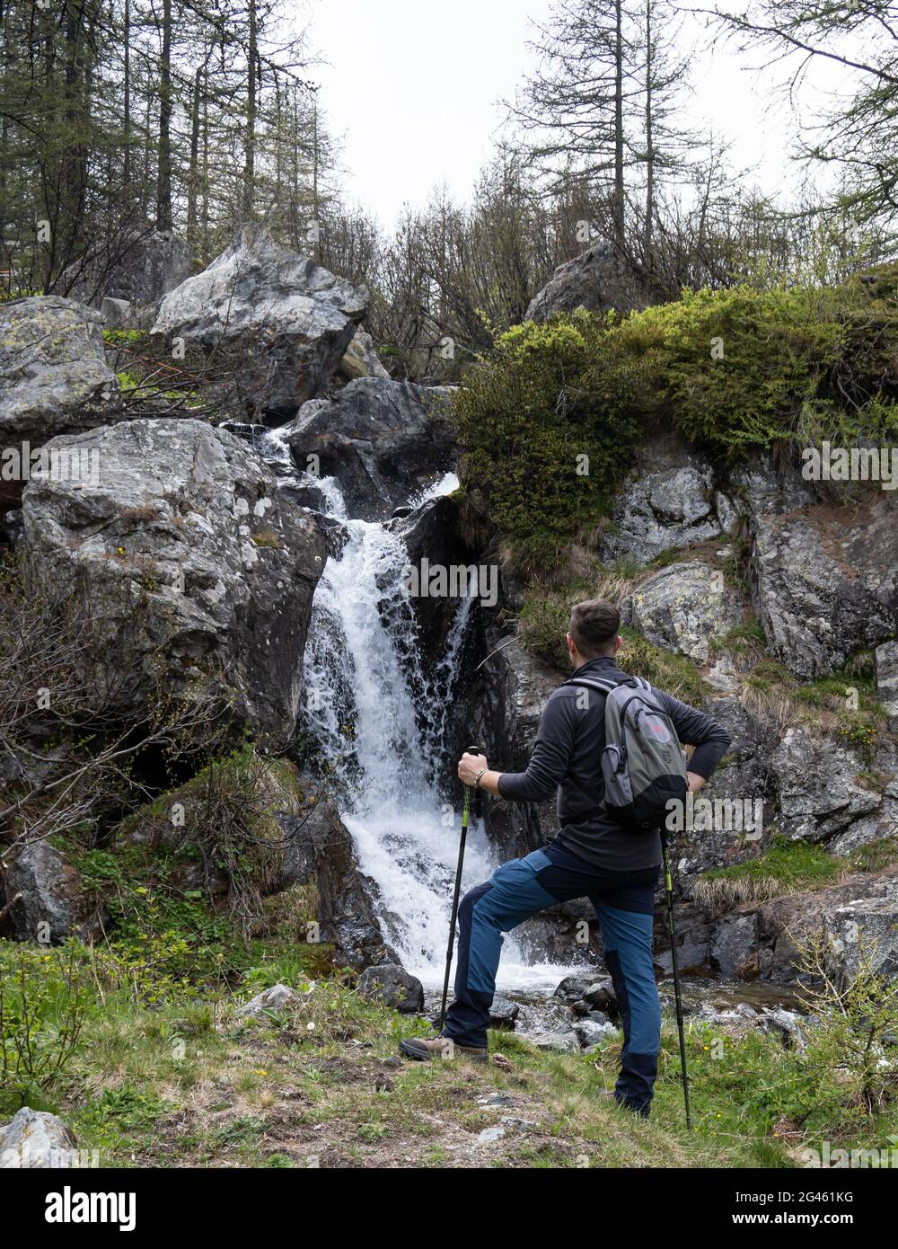 Ein junger Wanderer beobachtet den kleinen Wasserfall aus kristallklarem Wasser. Stockfoto