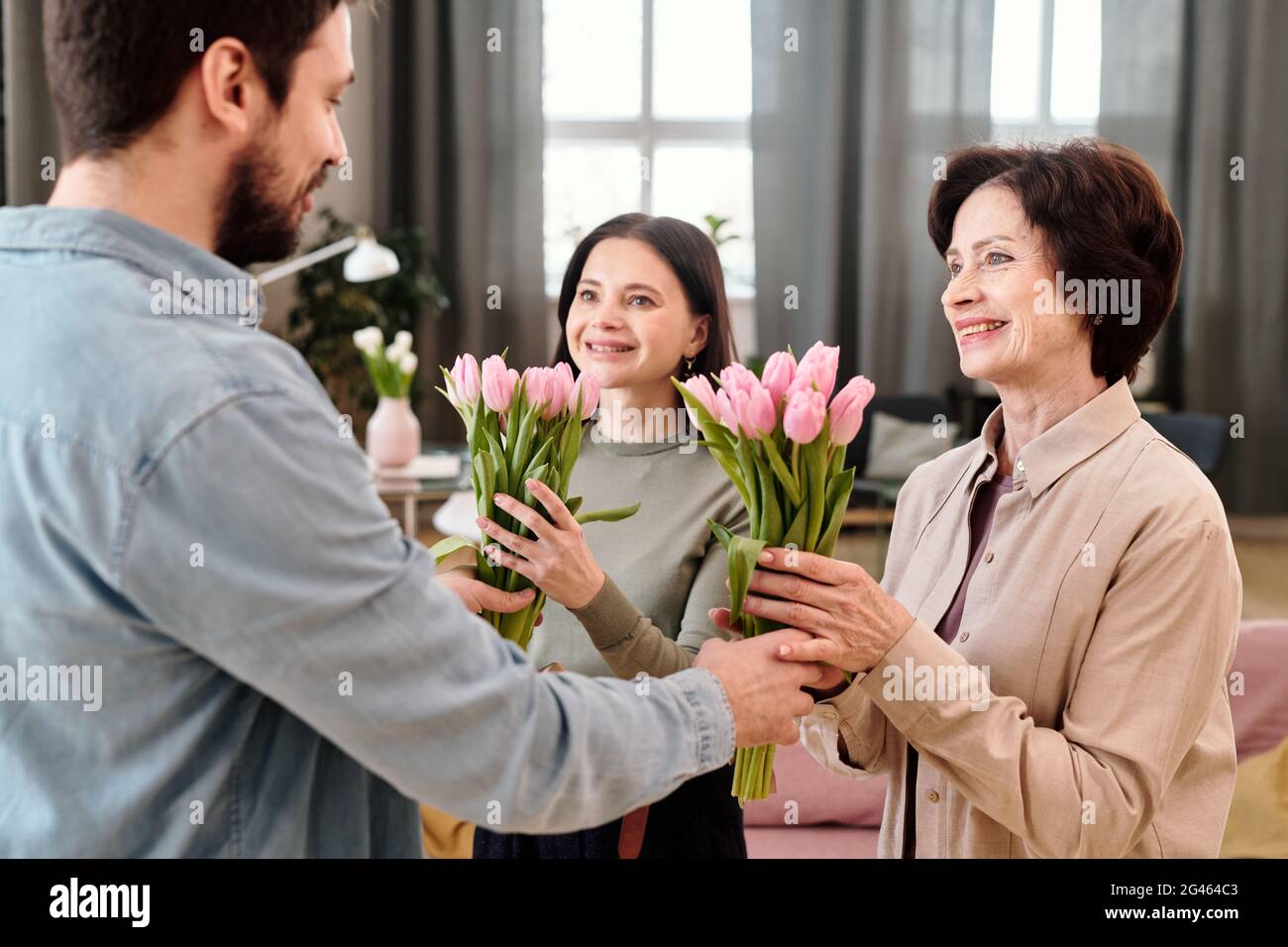 Fröhliche Weibchen mit Tulpen, die einen netten jungen Mann angupfen Stockfoto