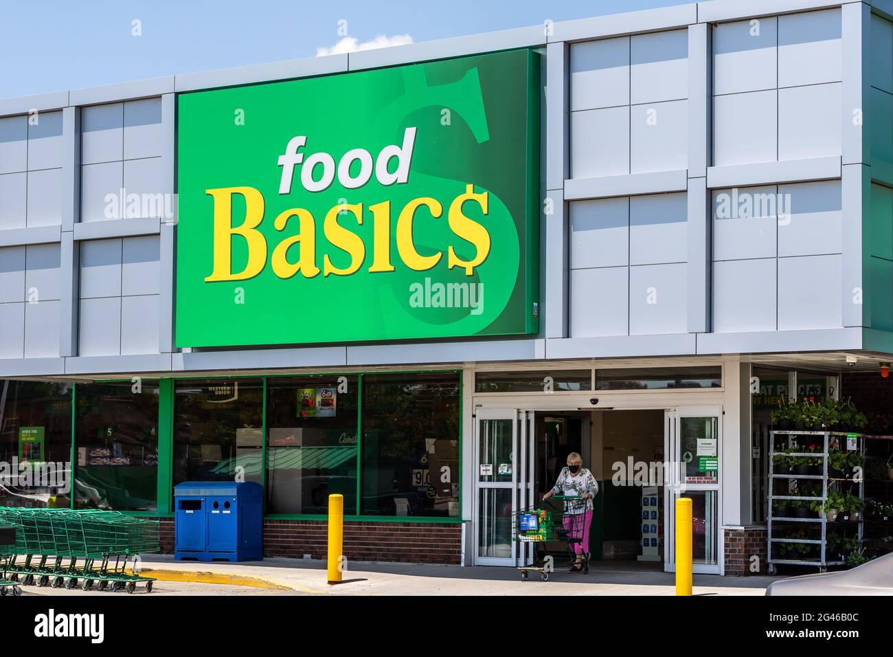 Strathroy, Ontario, Kanada: 11 2021. Juni: Lebensmittelgeschäft „Food Basics“ Schild. Ältere grauhaarige Frau, die einen Wagen schiebt und den Laden verlässt. Stockfoto