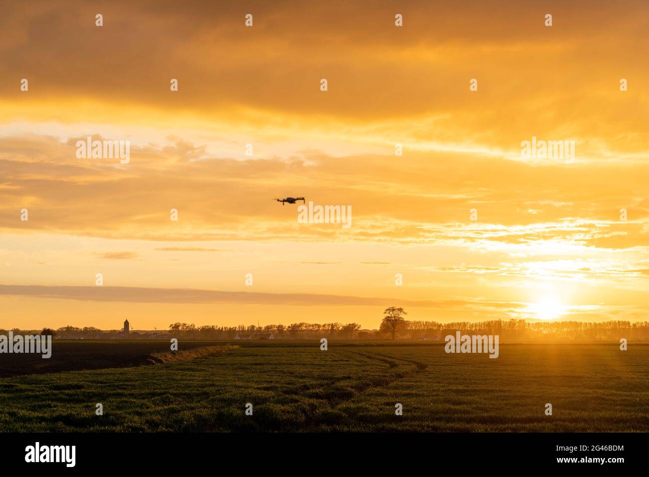 Eine Drohne, die über grüne Frühlingswiesen mit einem bunten fliegt Orangefarbener Sonnenuntergang am Himmel Stockfoto