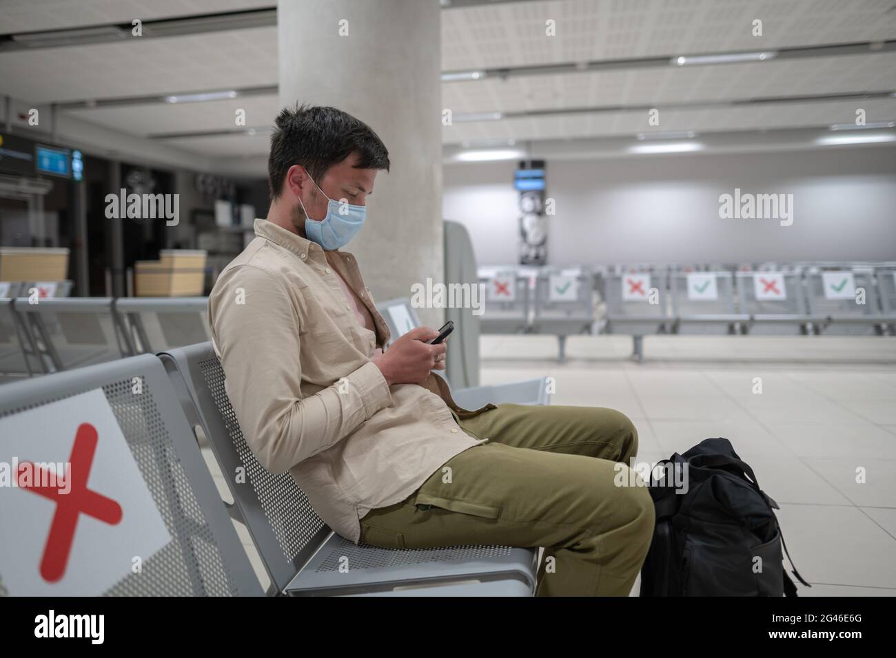 Der Mann, der eine Schutzmaske trägt, verärgert über den Annullierungsflug, schreibt eine Nachricht an seine Familie und sitzt im leeren Terminal am Flughafen von Stockfoto