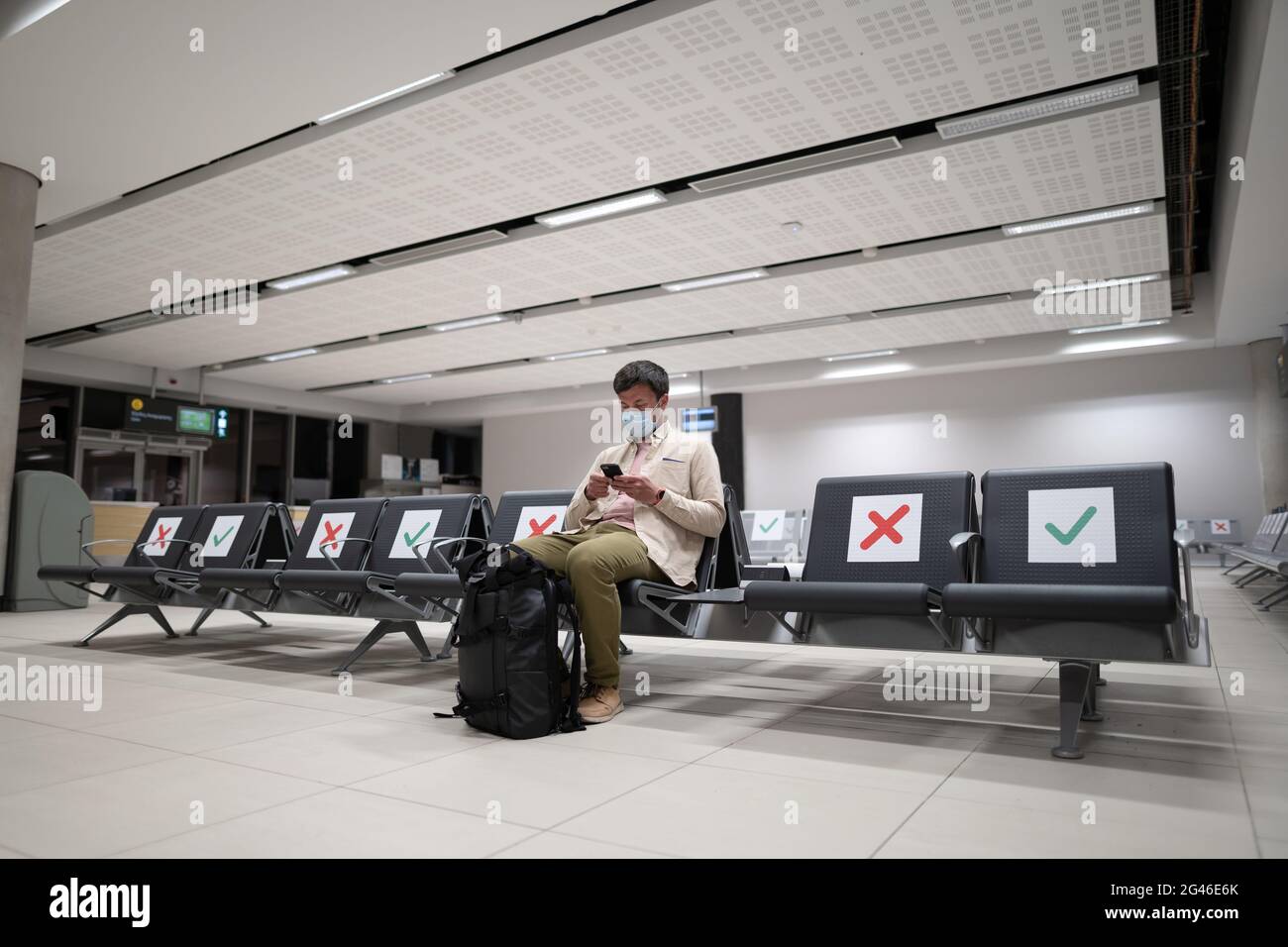Der Mann, der eine Schutzmaske trägt, verärgert über den Annullierungsflug, schreibt eine Nachricht an seine Familie und sitzt im leeren Terminal am Flughafen von Stockfoto