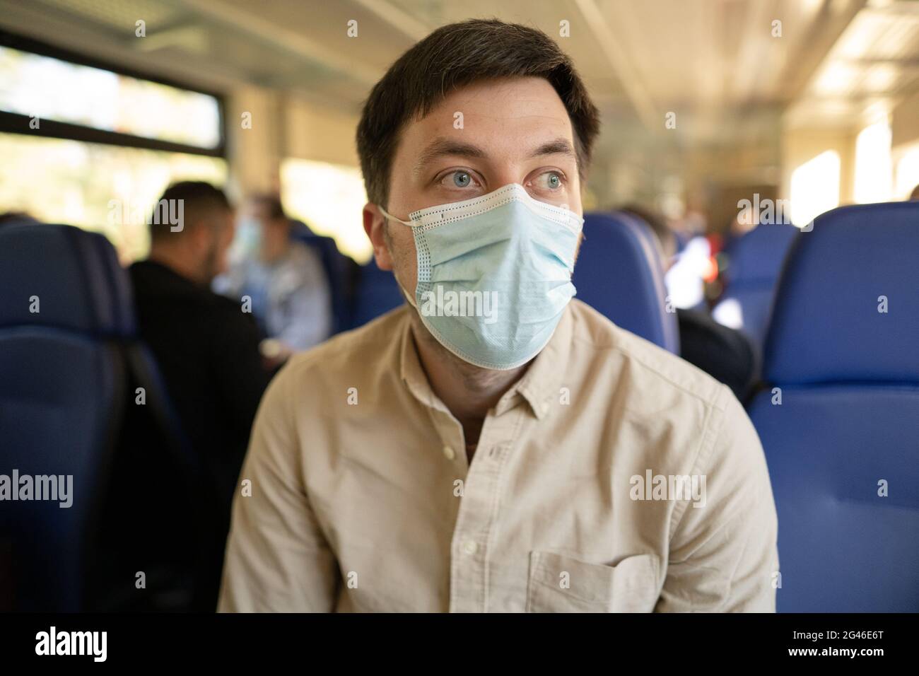 Mann, der mit dem Zug unterwegs ist und eine Gesichtsmask trägt. Soziale Distanzierung bei Bahnreisen während der Covid-19-Pandemie. Männlich pendeln nach Stockfoto