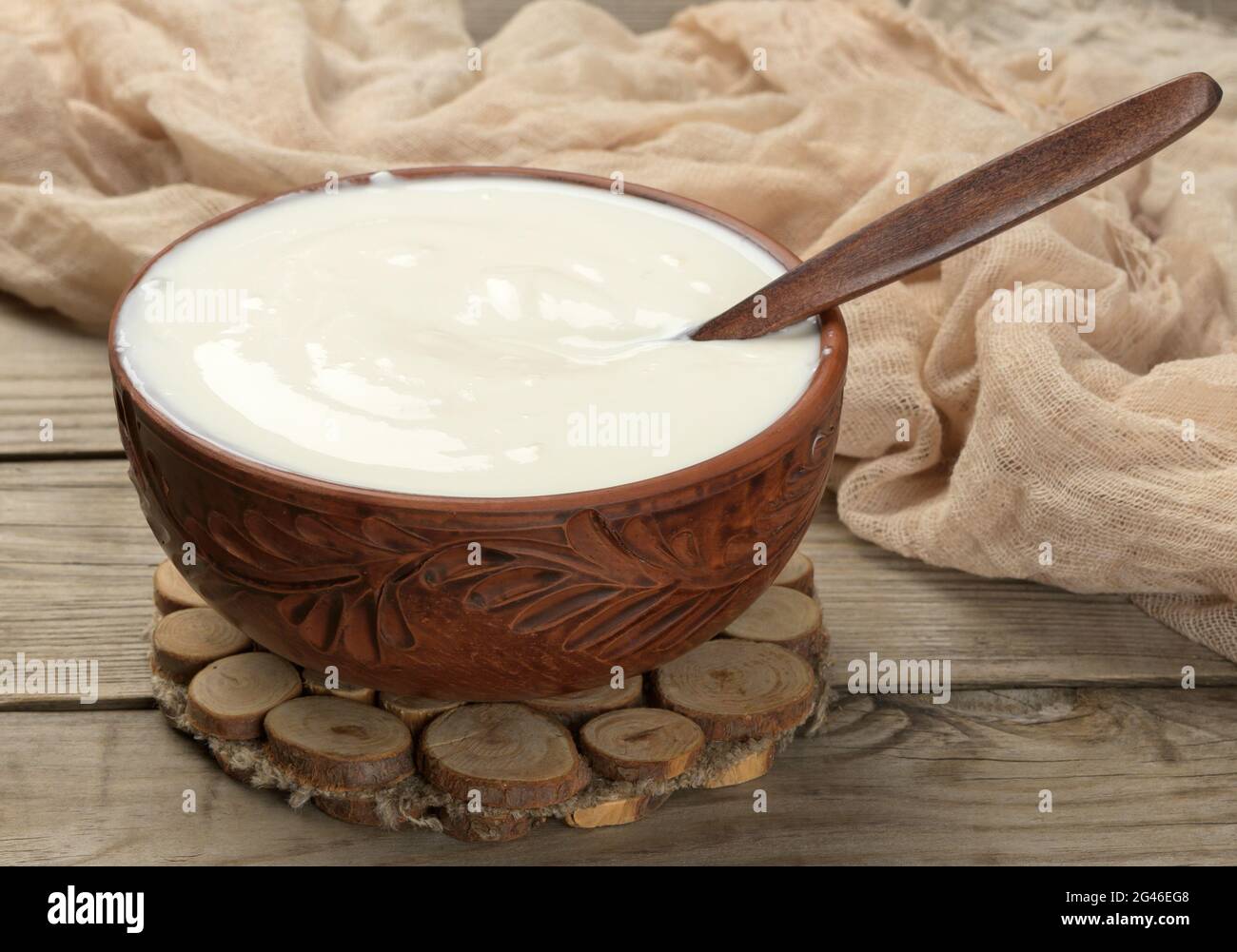 Saure Creme in einer braunen Keramikschale mit einem Holzlöffel auf einem hölzernen Hintergrund, fermentierte Milch nützliches Produkt Stockfoto