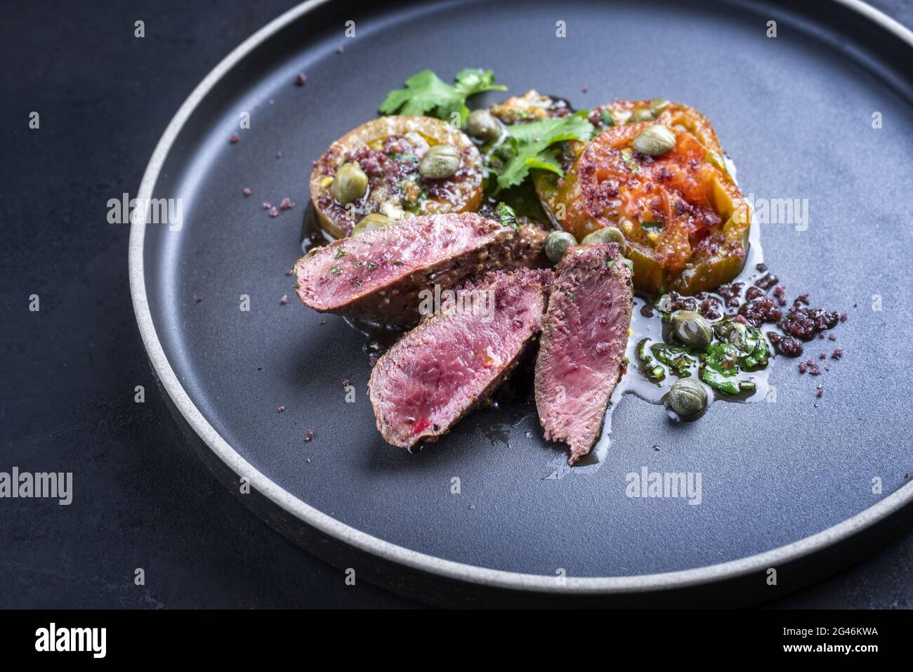 Traditionelles Wildhasenrückenfilet im modernen Stil, geschmort mit Tomatenscheiben und Kapern in Kräuterjus, serviert als Nahaufnahme auf einem nordischen d Stockfoto