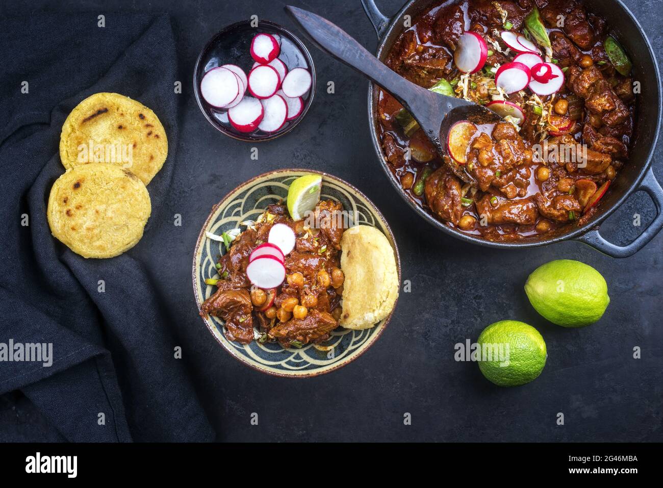 Traditionelles, langsam gekochtes mexikanisches Pozole rojo mit Tortilla serviert als Draufsicht in einem gusseisernen Bräter im modernen Design auf einem rus Stockfoto