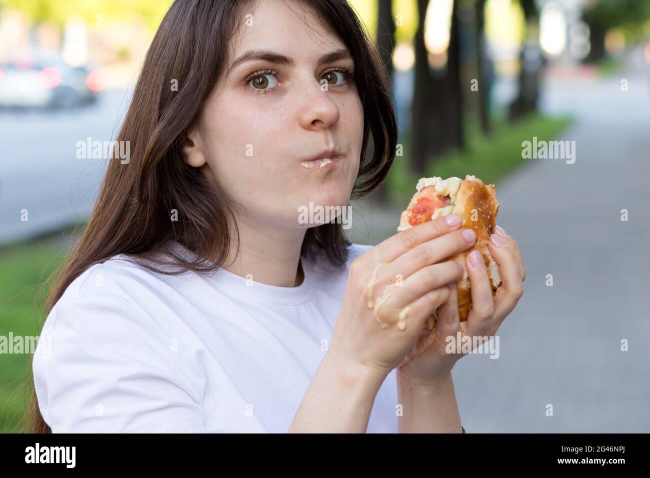 Brünette Frau überfrisst auf einem Burger auf der Straße. Völlerei, überschüssige Kalorien und Bulimie. Stockfoto