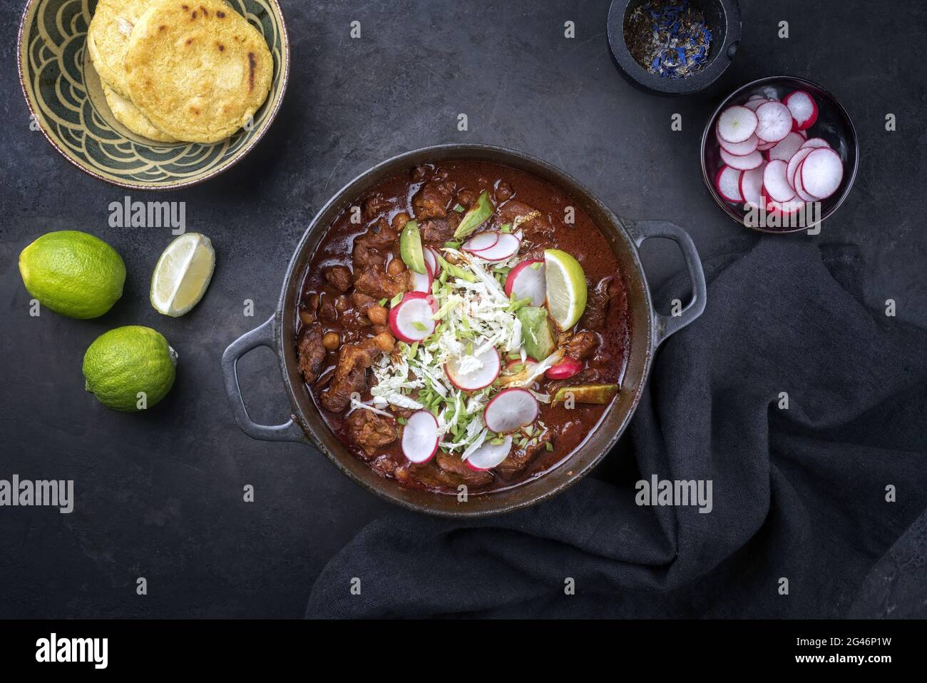 Traditionelles, langsam gekochtes mexikanisches Pozole rojo mit Tortilla serviert als Draufsicht in einem gusseisernen Bräter im modernen Design auf einem rus Stockfoto