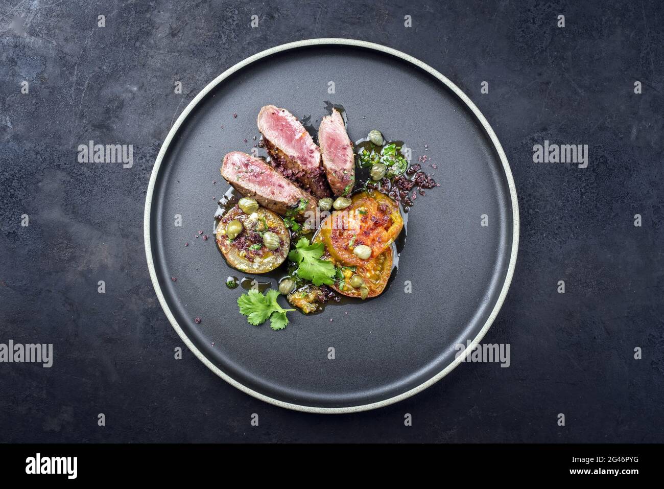 Traditionelles Wildhasenrückenfilet im modernen Stil, geschmort mit Tomatenscheiben und Kapern in Kräuterjus, serviert als Draufsicht auf einem nordischen d Stockfoto