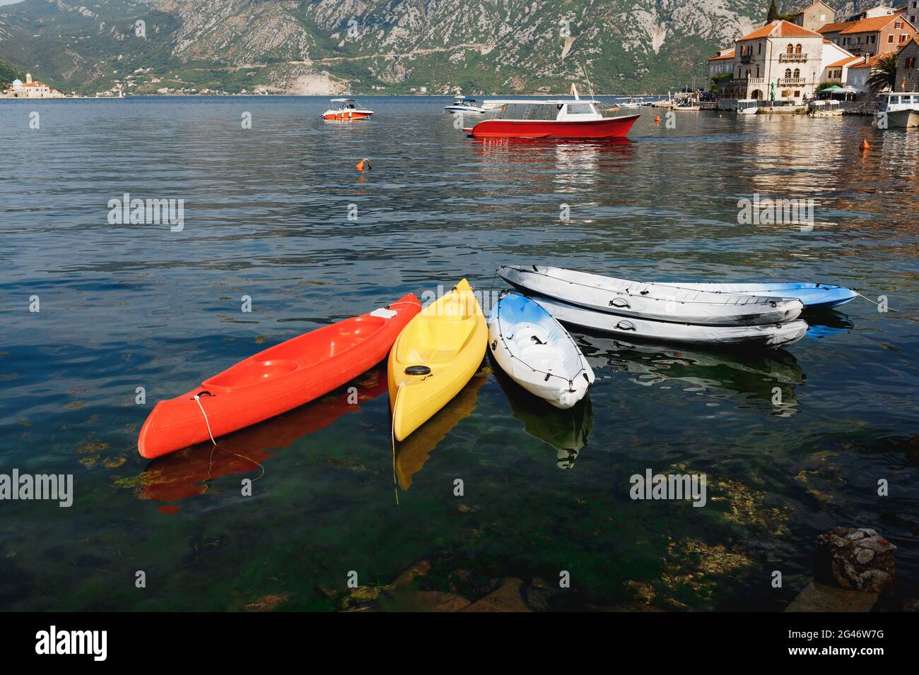 Sechs Kajaks, die in der Nähe der Küste in der Stadt Perast, Montenegro, festgemacht sind. Kajak rot, gelb, weiß-blau Stockfoto